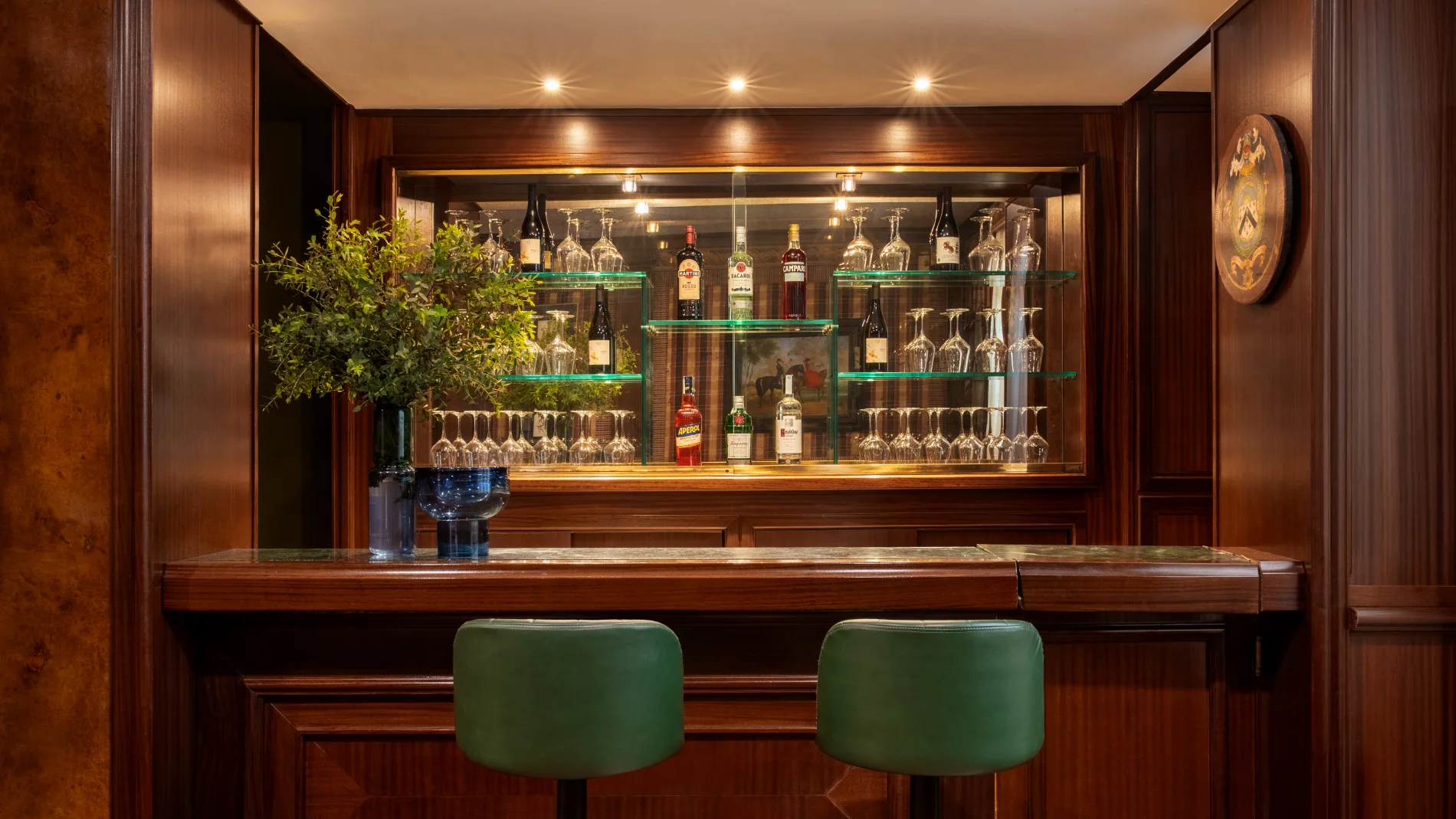 Wood-panelled bar with green stools, illuminated cabinet, bottles and glasses in central Rome - The Hotel Britannia, BZAR hotels in Rome