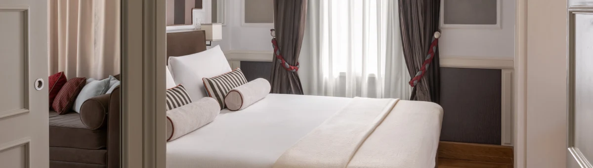 Panoramic room with double bed, sofa, grey curtains and French doors opening to a terrace in Rome - The Hotel Britannia, BZAR hotels in Rome