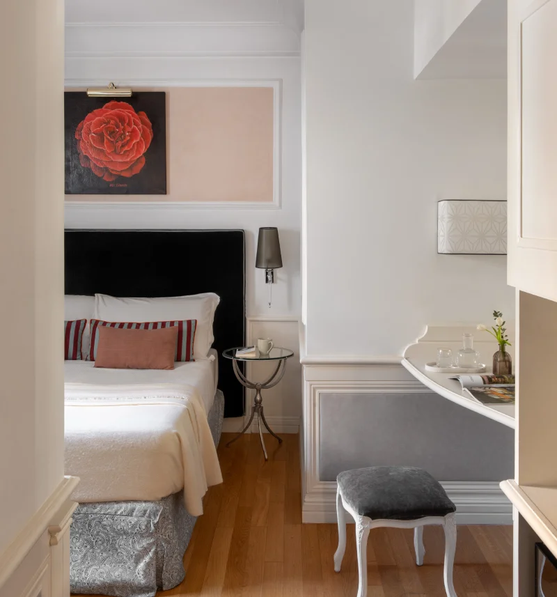 Bright room with double bed, red floral artwork, vanity desk and stool in central Rome - The Hotel Britannia, BZAR hotels in Rome