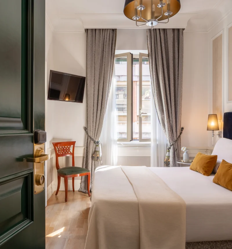 Room with open green door, double bed, bright window, TV and wooden chair near the Rome Opera House - The Hotel Britannia, BZAR hotels in Rome