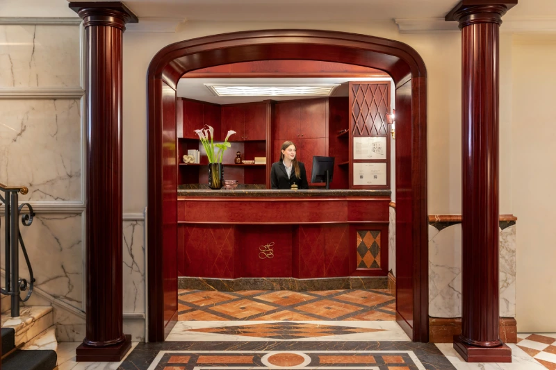 Elegant reception with red desk, wood columns, marble details and staff near Piazza della Repubblica - The Hotel Britannia, BZAR hotels in Rome